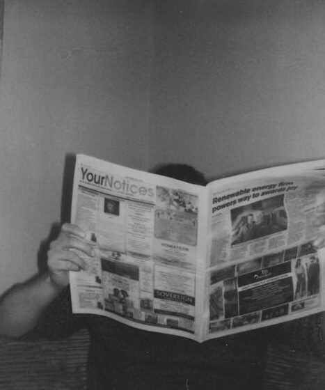 Person reading a newspaper at home in a vintage black and white style.